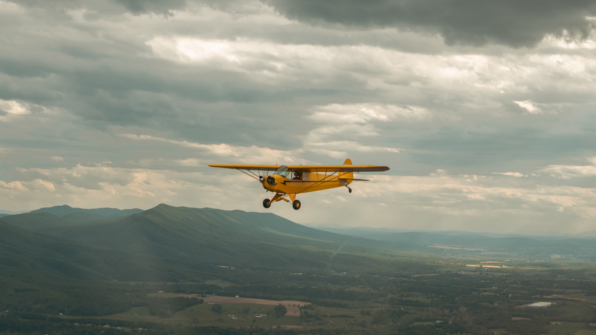 A piper J3 Cub airplane flying high above the Massanutten mountains in Virginia.